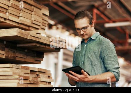 Ich habe für diese Woche viele Bestellungen anstehen. Ausgeschnittene Aufnahme eines jungen Zimmermanns mit einem digitalen Tablet, während er in seiner Werkstatt arbeitete. Stockfoto