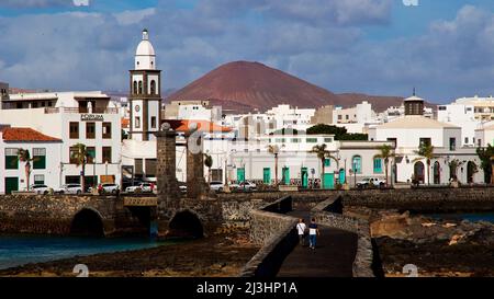 Kanarische Inseln, Lanzarote, Vulkaninsel, Hauptstadt Arrecife, Blick von der Brücke Puente de las Bolas nach Arrecife und zur Kirche Parroquia de San Ginés, im Hintergrund ein rötlich-blauer Lavabügel mit vielen grau-weißen Wolken Stockfoto