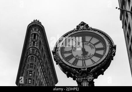 23 Street, New York City, NY, USA, Historic Flatiron or Fuller Building, ein 22-stöckiges, dreieckiges, stahlgerahmtes Wahrzeichen, das 1902 erbaut wurde und als einer der ersten Wolkenkratzer aller Zeiten und eine der berühmten New Yorker Straßenuhren gilt Stockfoto