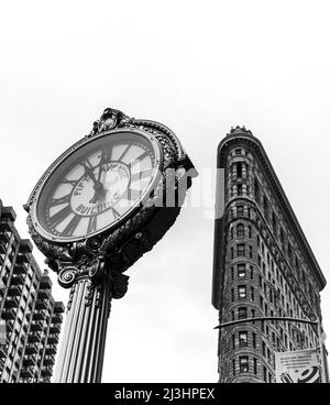23 Street, New York City, NY, USA, Historic Flatiron or Fuller Building, ein 22-stöckiges, dreieckiges, stahlgerahmtes Wahrzeichen, das 1902 erbaut wurde und als einer der ersten Wolkenkratzer aller Zeiten und eine der berühmten New Yorker Straßenuhren gilt Stockfoto