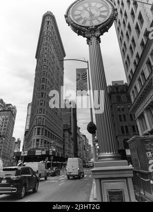 23 Street, New York City, NY, USA, Historic Flatiron or Fuller Building, ein 22-stöckiges, dreieckiges, stahlgerahmtes Wahrzeichen, das 1902 erbaut wurde und als einer der ersten Wolkenkratzer aller Zeiten und eine der berühmten New Yorker Straßenuhren gilt Stockfoto