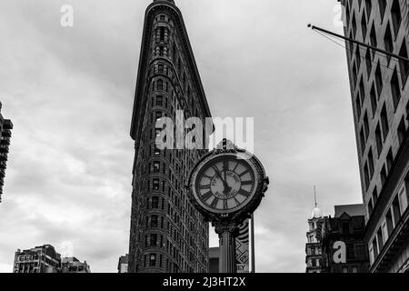 23 Street, New York City, NY, USA, Historic Flatiron or Fuller Building, ein 22-stöckiges, dreieckiges, stahlgerahmtes Wahrzeichen, das 1902 erbaut wurde und als einer der ersten Wolkenkratzer aller Zeiten und eine der berühmten New Yorker Straßenuhren gilt Stockfoto