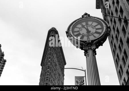 23 Street, New York City, NY, USA, Historic Flatiron or Fuller Building, ein 22-stöckiges, dreieckiges, stahlgerahmtes Wahrzeichen, das 1902 erbaut wurde und als einer der ersten Wolkenkratzer aller Zeiten und eine der berühmten New Yorker Straßenuhren gilt Stockfoto