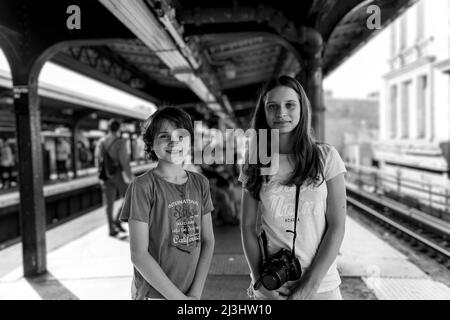 Myrtle AV, New York City, NY, USA, 14 Jahre altes kaukasisches Teenager-Mädchen und 12 Jahre altes kaukasisches Teenager-Mädchen – beide mit braunen Haaren und sommerlichem Styling warten an einer U-Bahn-Station in Brooklyn auf die U-Bahn Stockfoto