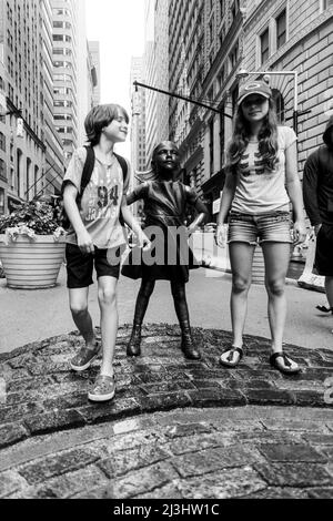 Finanzdistrikt, New York City, NY, USA, 14 Jahre altes kaukasisches Teenager-Mädchen und 12 Jahre altes kaukasisches Teenager-Mädchen – beide mit braunen Haaren und sommerlichem Styling neben der Statue „Fearless Girl“ von Kristen Visbal in der Broad Street vor der New Yorker Börse Stockfoto