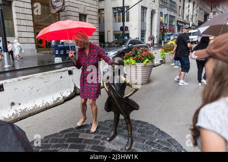 Financial District, New York City, NY, USA, Eine Dame mit einem Regenschirm, der neben der Statue „Fearless Girl“ von Kristen Visbal auf der Broad Street vor der New Yorker Börse steht Stockfoto