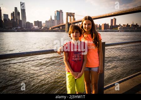 Dumbo/FULTON FERRY, New York City, NY, USA, 14 Jahre altes kaukasisches Teenager-Mädchen und 12 Jahre altes kaukasisches Teenager-Mädchen - beide mit braunen Haaren und sommerlichem Styling vor der Brooklyn Bridge über dem East River Stockfoto