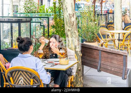 Zwei junge Frauen, die im Winter in Madrid, Spanien, Bier im Café im Freien genießen. Calle Serrano. Stockfoto