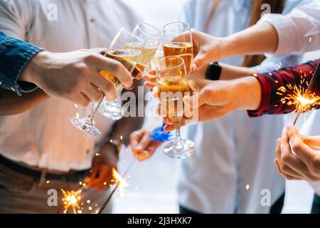 Nahaufnahme ist ein nicht erkennbares, erfolgreiches Geschäftsteam aus jungen, multirassischen Geschäftsleuten, die bengalische Lichter und knallende Gläser Champagner halten. Stockfoto