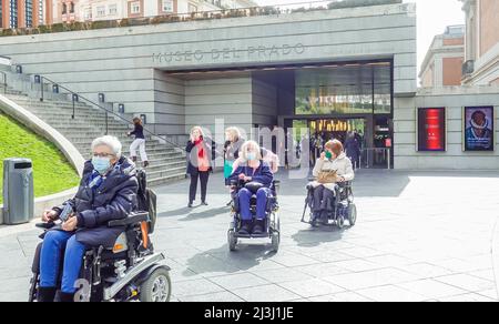 Ältere Seniorinnen in Rollstühlen in Gesichtsmasken, die das Prado-Museum verlassen. Frau in einem motorisierten elektrischen Rollstuhl-Mobilitätsgerät. Madrid, Spanien Stockfoto