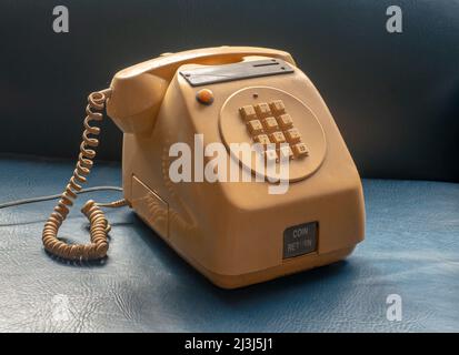 Alte Tischversion münzbetriebenes öffentliches Telefon, wie es in Bars und Geschäften verwendet wird, gelb auf blauem Hintergrund. Stockfoto