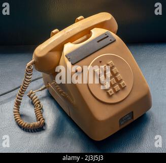 Alte Tischversion münzbetriebenes öffentliches Telefon, wie es in Bars und Geschäften verwendet wird, gelb auf blauem Hintergrund. Stockfoto