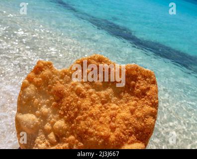 Johnnys Kuchen oder Yaniqueque, ein in der Dominikanischen Republik gebratenes Brot, im Hintergrund ein jungfräulicher Strand Stockfoto