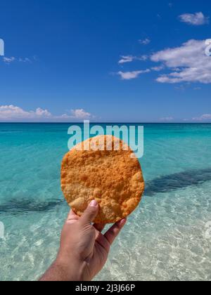 Johnnys Kuchen oder Yaniqueque, ein in der Dominikanischen Republik gebratenes Brot, im Hintergrund ein jungfräulicher Strand Stockfoto