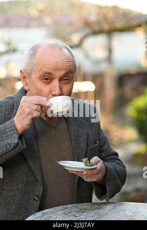 Porträt eines lächelnden grauhaarigen Mannes, der im Garten steht und Kaffee trinkt Stockfoto