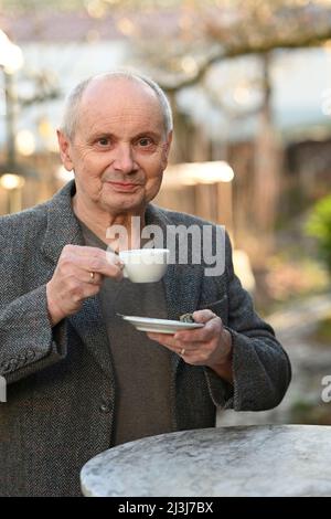 Porträt eines lächelnden grauhaarigen Mannes, der im Garten steht und Kaffee trinkt Stockfoto