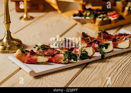 Prosciutto mit Gorgonzola und Birne Sommer-Snacks. Birnenvorspeise mit Jamon, Rucola und Brie Cheese auf schwarzem Tisch Stockfoto
