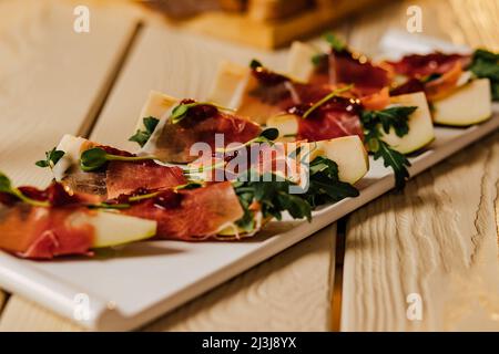 Prosciutto mit Gorgonzola und Birne Sommer-Snacks. Birnenvorspeise mit Jamon, Rucola und Brie Cheese auf schwarzem Tisch. Stockfoto