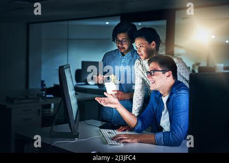 Arbeiten in der Spätschicht. Aufnahme einer Gruppe von Programmierern, die in der Nacht im Büro an einem Computer arbeiten. Stockfoto
