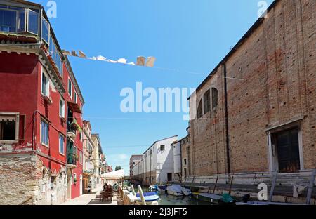 Wäscheleinen zwischen einer Kirche und Häusern mit Kleidung über dem schiffbaren Kanal auf der Insel Venedig in Italien Stockfoto