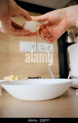 Nahaufnahme Frau Hände brechen Hühnereier in einem Teller in der Küche. Teig kochen. Stockfoto
