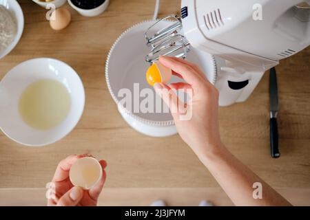 Nahaufnahme Frau Hände brechen Hühnereier in einem Teller in der Küche. Teig kochen. Stockfoto