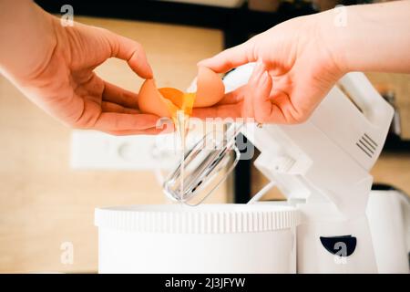 Nahaufnahme Hände brechen Hühnereier in einer Rührschüssel in der Küche. Teig kochen. Stockfoto