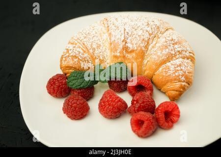 Appetitliche knusprige Croissants und frische Himbeeren auf einem weißen Teller. Französisches Frühstück. Frisch duftendes Gebäck und Himbeeren. Hintergrund und SPA kopieren Stockfoto