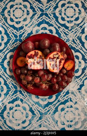 Stillleben rohe Pflaumen, Granatapfel und Trauben im Vintage-Hintergrund Stockfoto