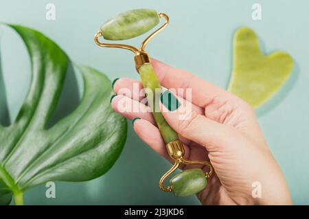 Weibliche Hand hält Massagerolle für das Gesicht mit zwei Köpfen aus grünem Stein Stockfoto