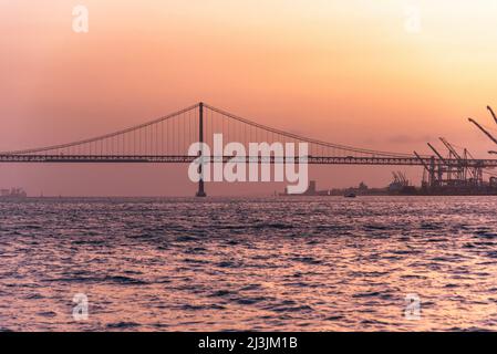 Die 25 de Abril Brücke supinsion Brücke von Lissabon bei Sonnenuntergang. Wunderschöne rote und türkisfarbene Farben über dem Fluss Tejo Stockfoto