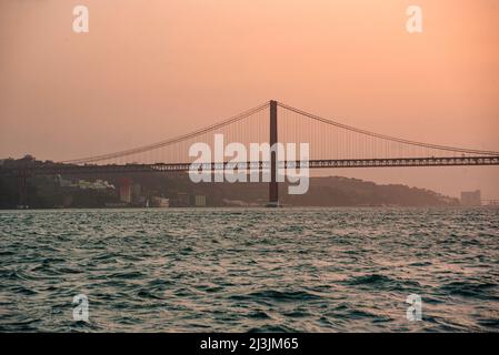 Die 25 de Abril Brücke supinsion Brücke von Lissabon bei Sonnenuntergang. Wunderschöne rote und türkisfarbene Farben über dem Fluss Tejo Stockfoto