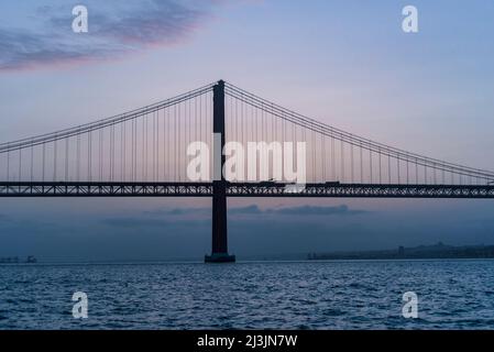 Die 25 de Abril Brücke supinsion Brücke von Lissabon bei Sonnenuntergang. Wunderschöne rote und türkisfarbene Farben über dem Fluss Tejo Stockfoto