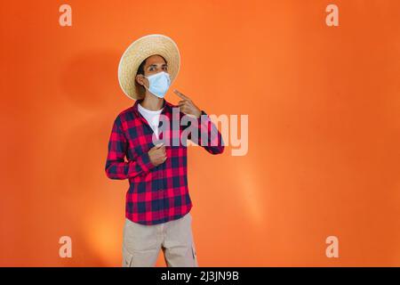 Schwarzer Mann mit Junina Party Outfit zeigt isoliert auf orangenen Hintergrund. Junger Mann in traditioneller Kleidung für Festa Junina - Brasilianischer Juni fe Stockfoto