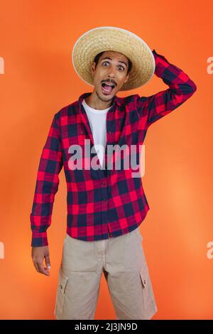 Schwarzer Mann mit Junina Party Outfit isoliert auf orangefarbenem Hintergrund. Junger Mann in traditioneller Kleidung für Festa Junina - brasilianisches Juni-Festival. Stockfoto