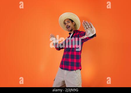 Schwarzer Mann mit Junina Party Outfit isoliert auf orangefarbenem Hintergrund. Junger Mann in traditioneller Kleidung für Festa Junina - brasilianisches Juni-Festival. Stockfoto