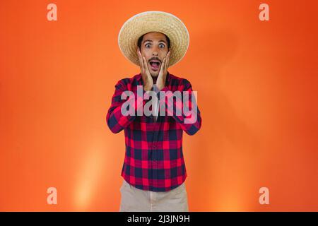 Schwarzer Mann mit Junina Party Outfit isoliert auf orangefarbenem Hintergrund. Junger Mann in traditioneller Kleidung für Festa Junina - brasilianisches Juni-Festival. Stockfoto