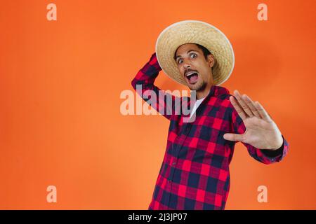 Schwarzer Mann mit Junina Party Outfit isoliert auf orangefarbenem Hintergrund. Junger Mann in traditioneller Kleidung für Festa Junina - brasilianisches Juni-Festival. Stockfoto