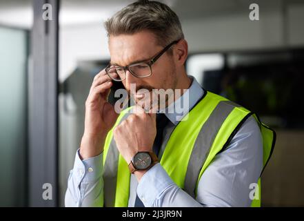 Das könnte tatsächlich funktionieren Eine kurze Aufnahme eines hübschen, reifen männlichen Bauarbeiters, der beim Anruf in seinem Büro nachdenklich aussachte. Stockfoto