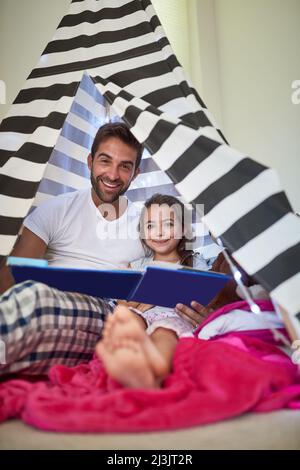 Es gibt nichts Wichtigeres als eine gute Zeit zusammen. Porträt eines Vaters, der mit seiner kleinen Tochter zu Hause in einem Zelt ein Buch liest. Stockfoto