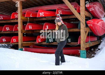 Eine lässige Frau, die vor einem Kajak-Rack steht, wo Kajaks und Kanus während des kanadischen Winters auf dem Rack andocken, und auf den Saisonstart wartet Stockfoto