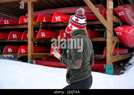 Eine lässige Frau, die vor einem Kajak-Rack steht, wo Kajaks und Kanus während des kanadischen Winters auf dem Rack andocken, und auf den Saisonstart wartet Stockfoto