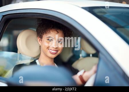 Fühlt sich gut an, auf dieser Seite des Autos zu sein. Beschnittenes Porträt einer attraktiven jungen Geschäftsfrau, die lächelt, während sie ihr neues Auto fährt. Stockfoto
