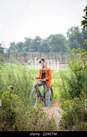 Porträt eines jungen Mannes, der auf seinem Fahrrad am Rande eines Grasfeldes sitzt und in die Kamera schaut; Nagli Village Noida, Noida, Uttar Pradesh, Indien Stockfoto