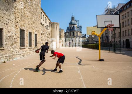 Junge Männer spielen Basketball im Innenhof hinter der Kirche Saint-Paul Saint-Louis in Le Marais, Paris, Frankreich Stockfoto