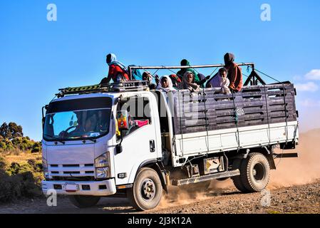 Die Menschen stehen auf dem Rücksitz eines Lastwagens, der auf einer staubigen, unbefestigten Straße im ländlichen Äthiopien, Äthiopien, unterwegs ist Stockfoto
