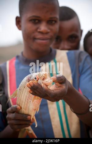 Ein kongolesischer Mann zeigt die Zähne eines Tigerfisches im Kongo; Bulu, Demokratische Republik Kongo. Stockfoto
