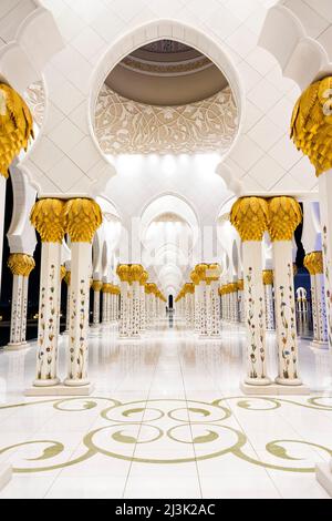 Ein Blick bei Nacht auf einen der kunstvoll verzierten Korridore der Großen Moschee in Abu Dhabi City, Vereinigte Arabische Emirate. Die Beschreibung lautet: "Wenn es wie Gold aussieht, dann... Stockfoto