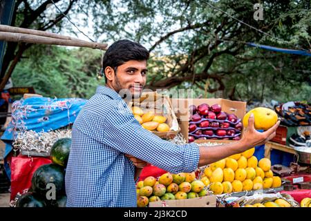 Junger Mann mit frischem Obst, um die Kamera auf einem Obstwagen im Freien zu zeigen, der frische Produkte verkauft; Großraum Noida, Uttar Pradesh, Indien Stockfoto
