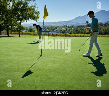 Den ganzen Tag über. Aufnahme von zwei jungen Männern, die draußen auf einem Golfplatz eine Partie Golf spielen. Stockfoto